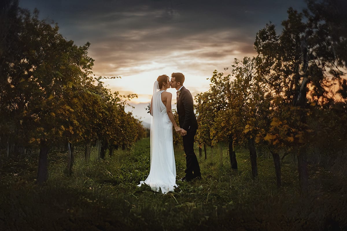 Fotografo matrimonio Torino. Matrimonio eco-consapevole a Cascina Ranverso. Ritratto degli sposi al tramonto. Sposi passeggiano nel vigneto e si baciano