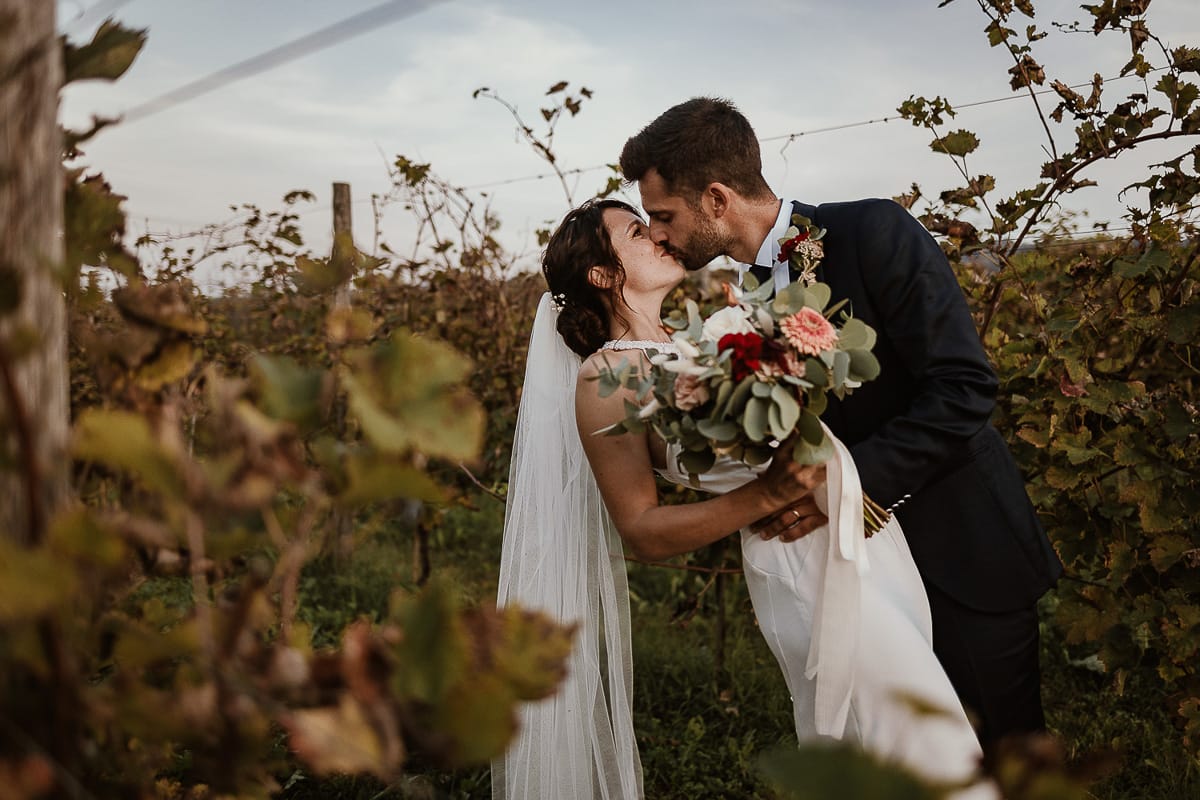 Fotografo matrimonio Torino. Matrimonio eco-consapevole a Cascina Ranverso. Ritratto degli sposi al tramonto. Sposi nel vigneto si baciano con un casquet