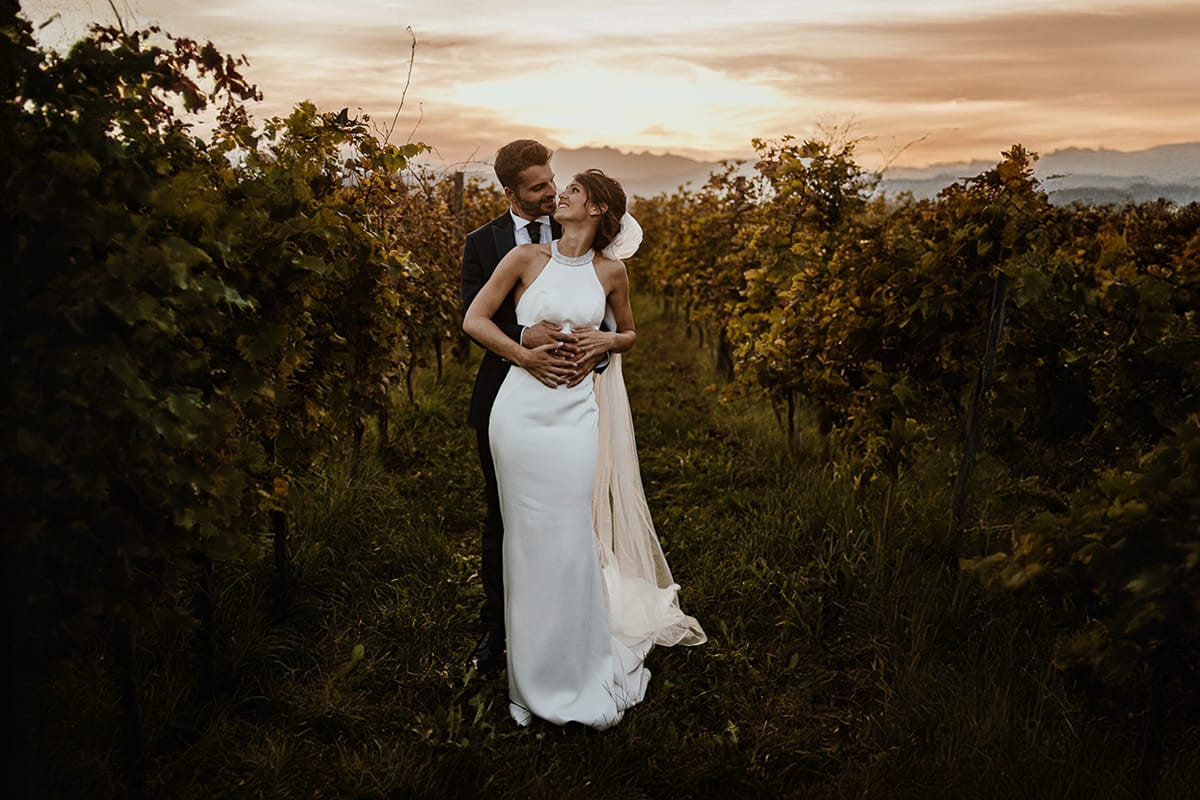 Fotografo matrimonio Torino. Matrimonio eco-consapevole a Cascina Ranverso. Ritratto degli sposi al tramonto. Sposi nel vigneto lo sposo abbraccia la sposa