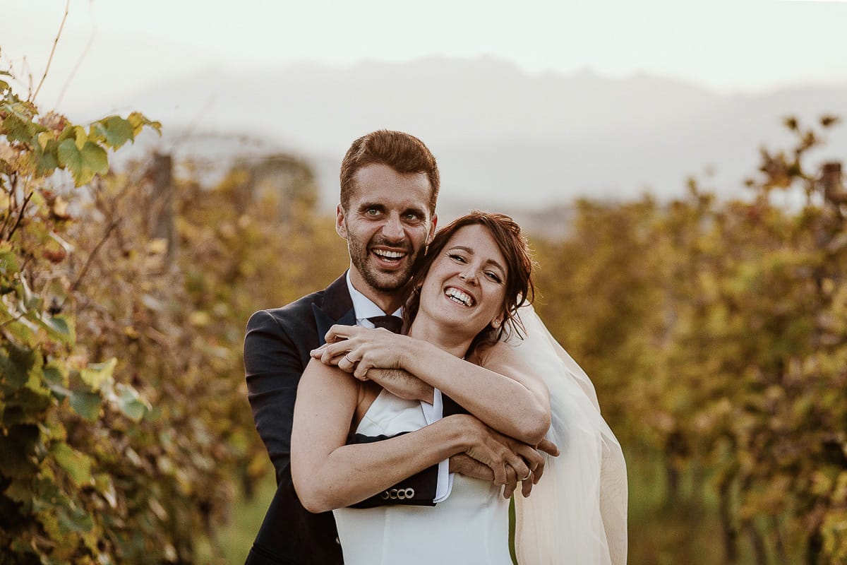 Fotografo matrimonio Torino. Matrimonio eco-consapevole a Cascina Ranverso. Ritratto degli sposi al tramonto. Sposi nel vigneto lo sposo abbraccia la sposa