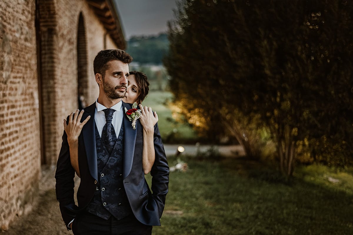 Fotografo matrimonio Torino. Matrimonio eco-consapevole a Cascina Ranverso. Ritratto degli sposi al tramonto. La sposa abbraccia lo sposo da dietro.