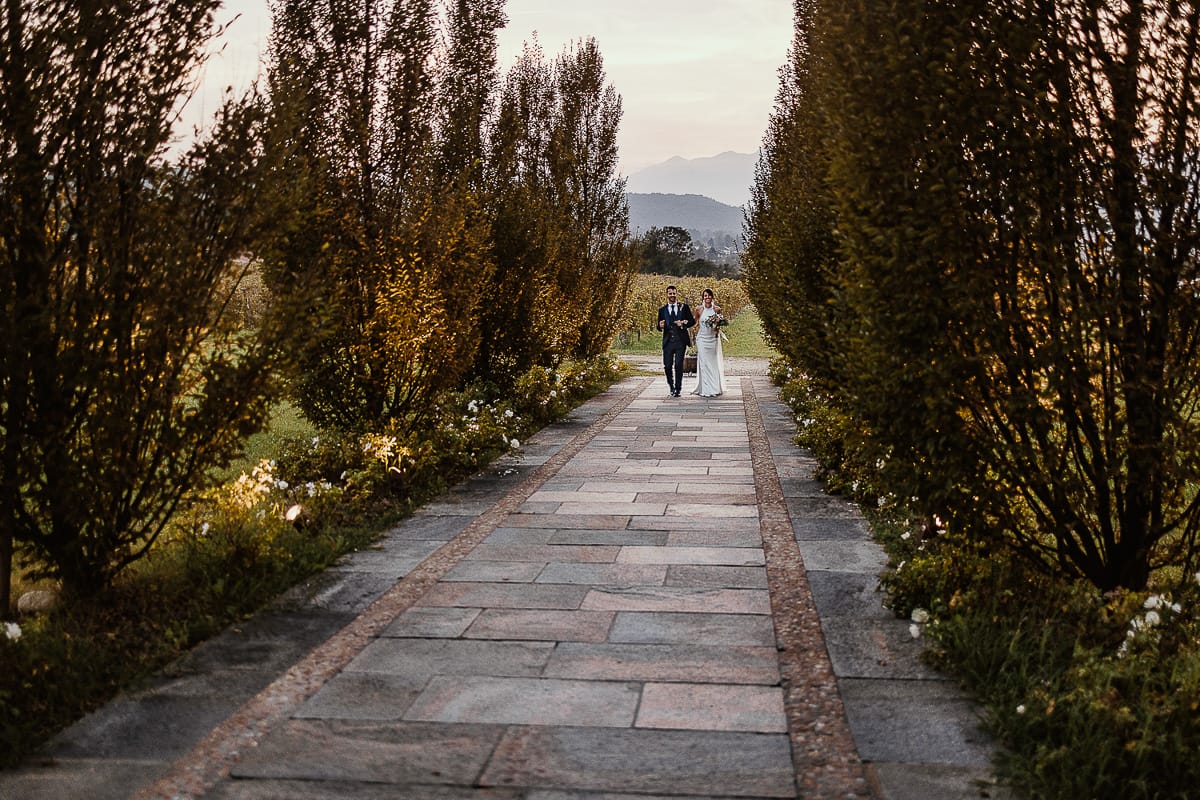 Fotografo matrimonio Torino. Matrimonio eco-consapevole a Cascina Ranverso. Ritratto degli sposi al tramonto. Gli sposi camminano sul viale che porta nella location