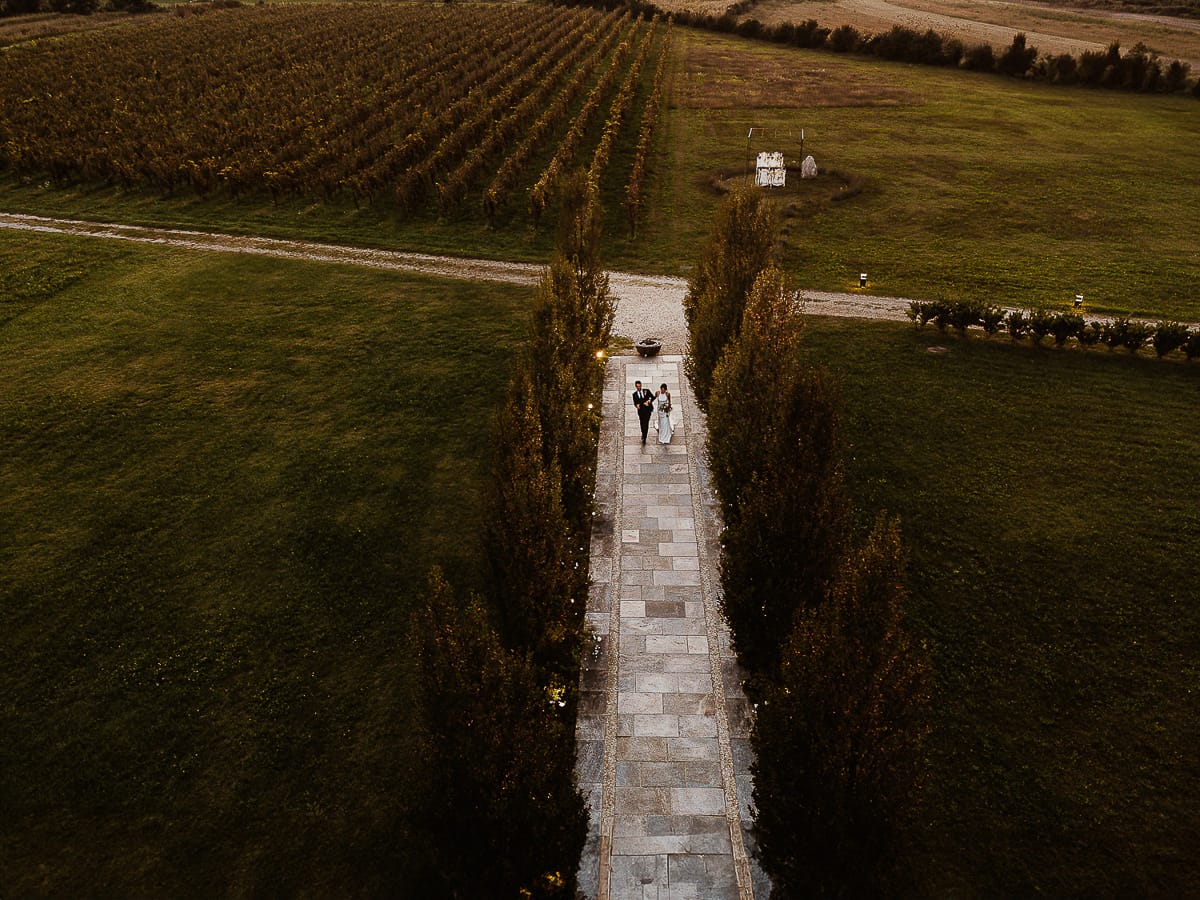 Fotografo matrimonio Torino. Matrimonio eco-consapevole a Cascina Ranverso. Ritratto degli sposi al tramonto. Gli sposi camminano sul viale che porta nella location Foto dal drone.