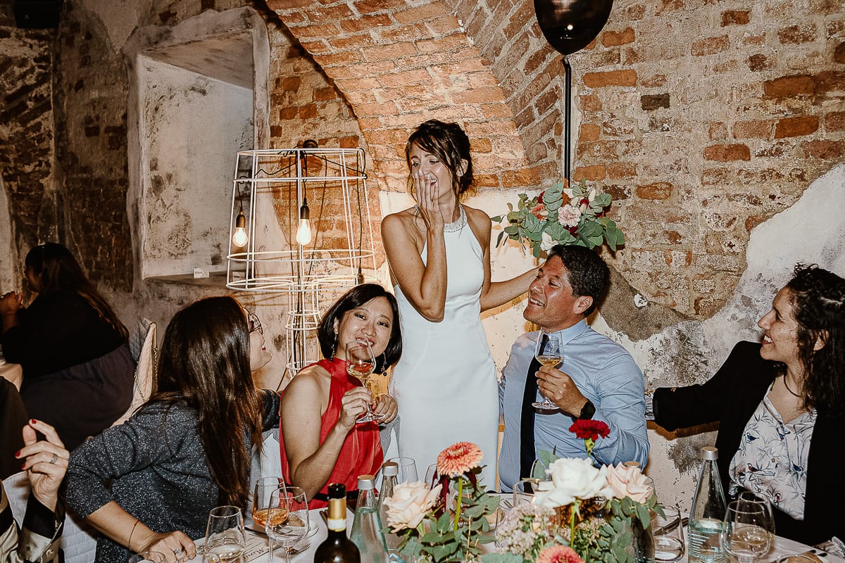 Fotografo matrimonio Torino. Matrimonio eco-consapevole a Cascina Ranverso. Cena. Sposa al tavolo con gli amici.