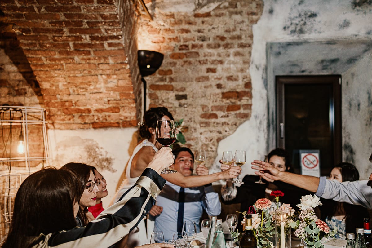 Fotografo matrimonio Torino. Matrimonio eco-consapevole a Cascina Ranverso. Cena. Sposa brinda al tavolo con gli amici