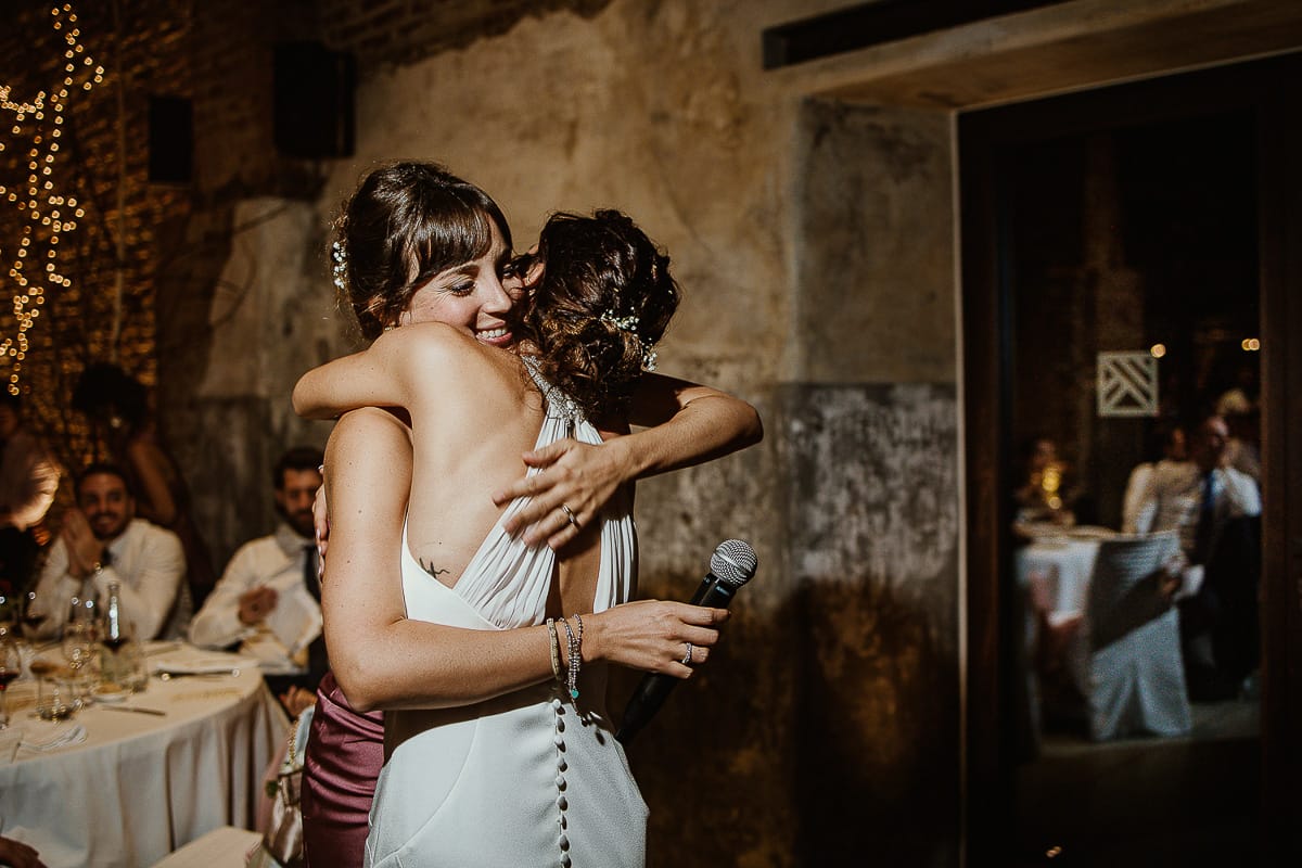 Fotografo matrimonio Torino. Matrimonio eco-consapevole a Cascina Ranverso. Cena. Discorso delle testimoni.Sposa abbraccia la testimone