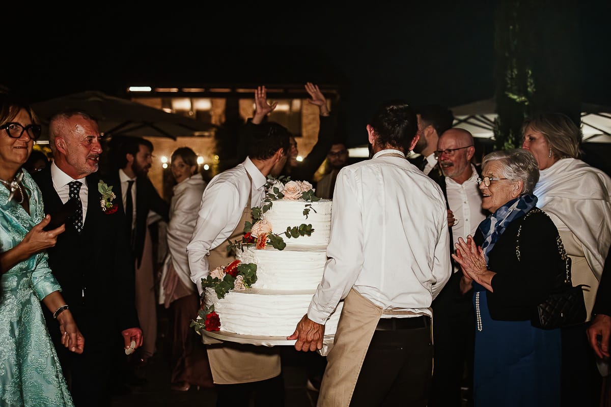 Fotografo matrimonio Torino. Matrimonio eco-consapevole a Cascina Ranverso. Taglio torta in esterno. I camerieri portano via la torta.