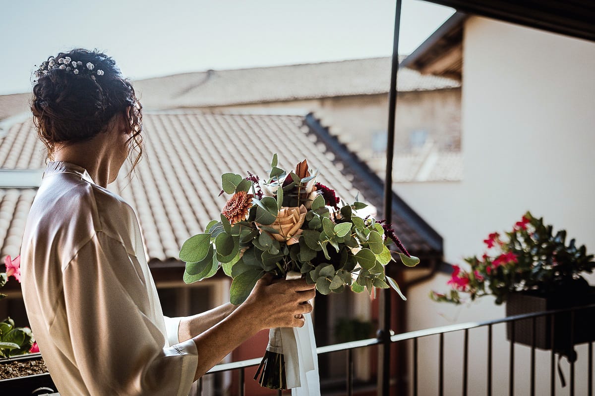 Fotografo matrimonio Torino. Matrimonio eco-consapevole a Cascina Ranverso. Preparazione della sposa a Chieri. Sposa sul balcone con il bouquet
