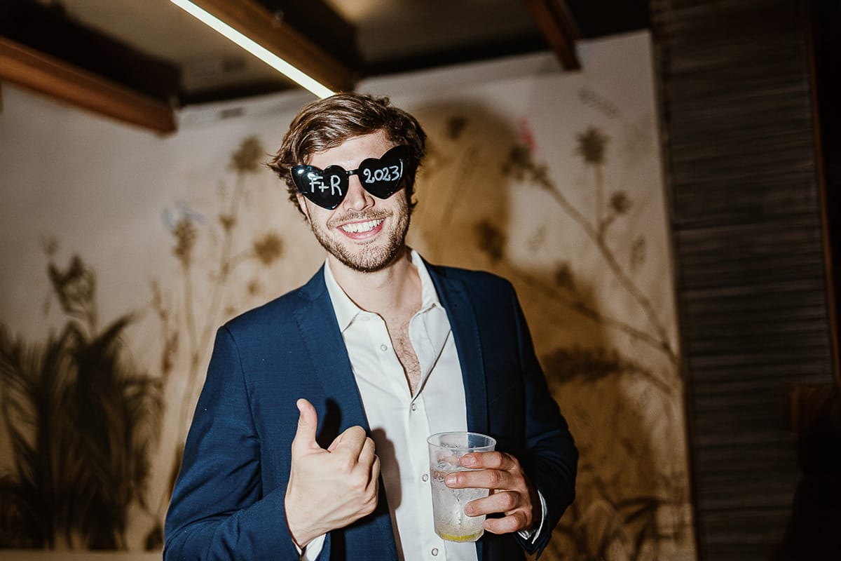 Fotografo matrimonio Torino.eco-consapevole a Cascina Ranverso. Festa. Invitato con occhiali a cuore con le iniziali degli sposi