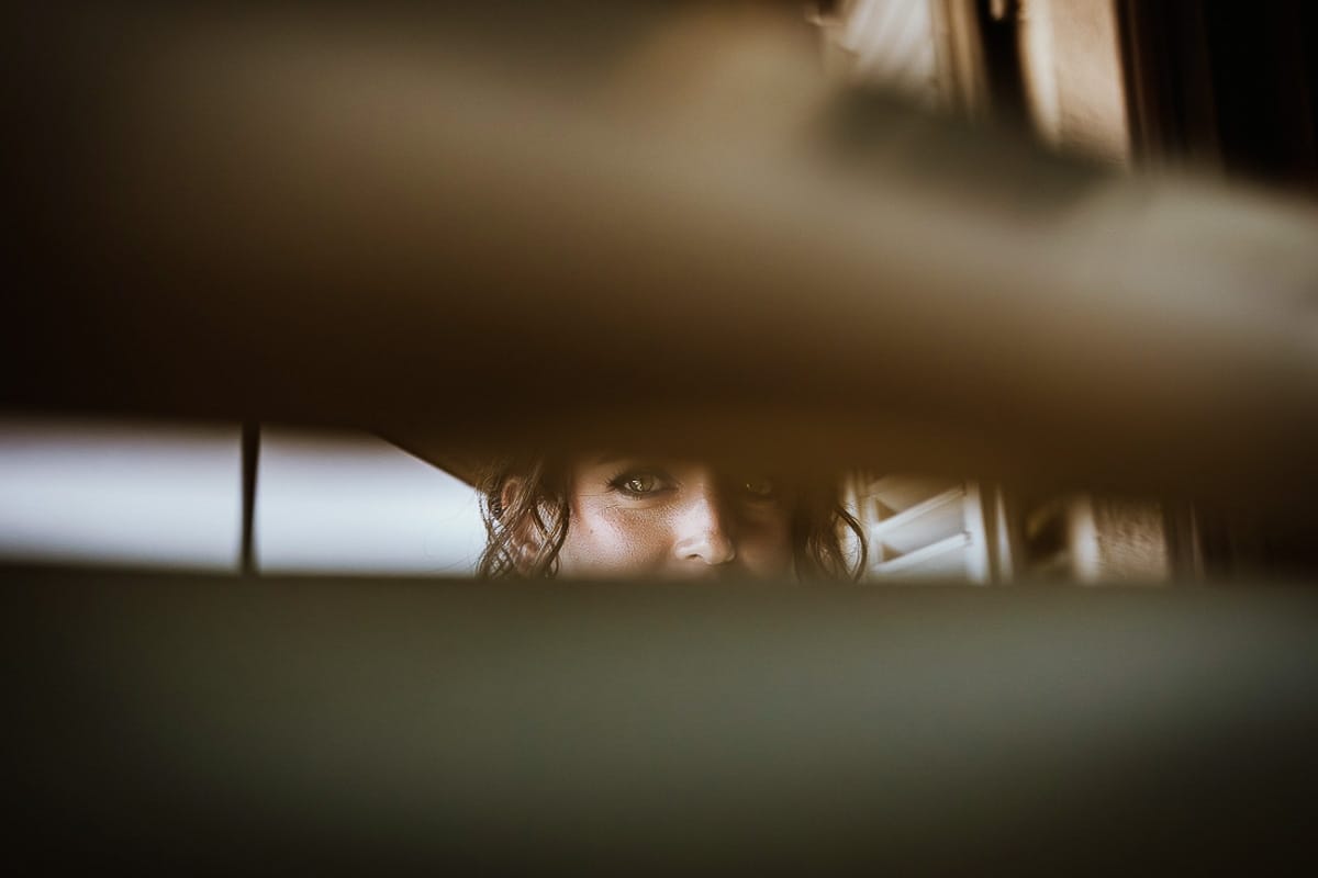 Fotografo matrimonio Torino. Matrimonio eco-consapevole a Cascina Ranverso. Preparazione della sposa a Chieri. Dettaglio degli occhi della sposa catturati attraverso le stecche della persiana.