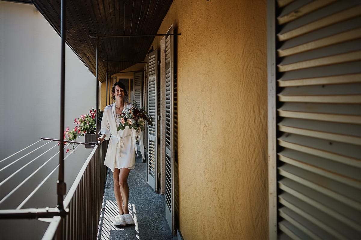 Fotografo matrimonio Torino. Matrimonio eco-consapevole a Cascina Ranverso. Preparazione della sposa a Chieri. Sposa cammina sul balcone con il bouquet