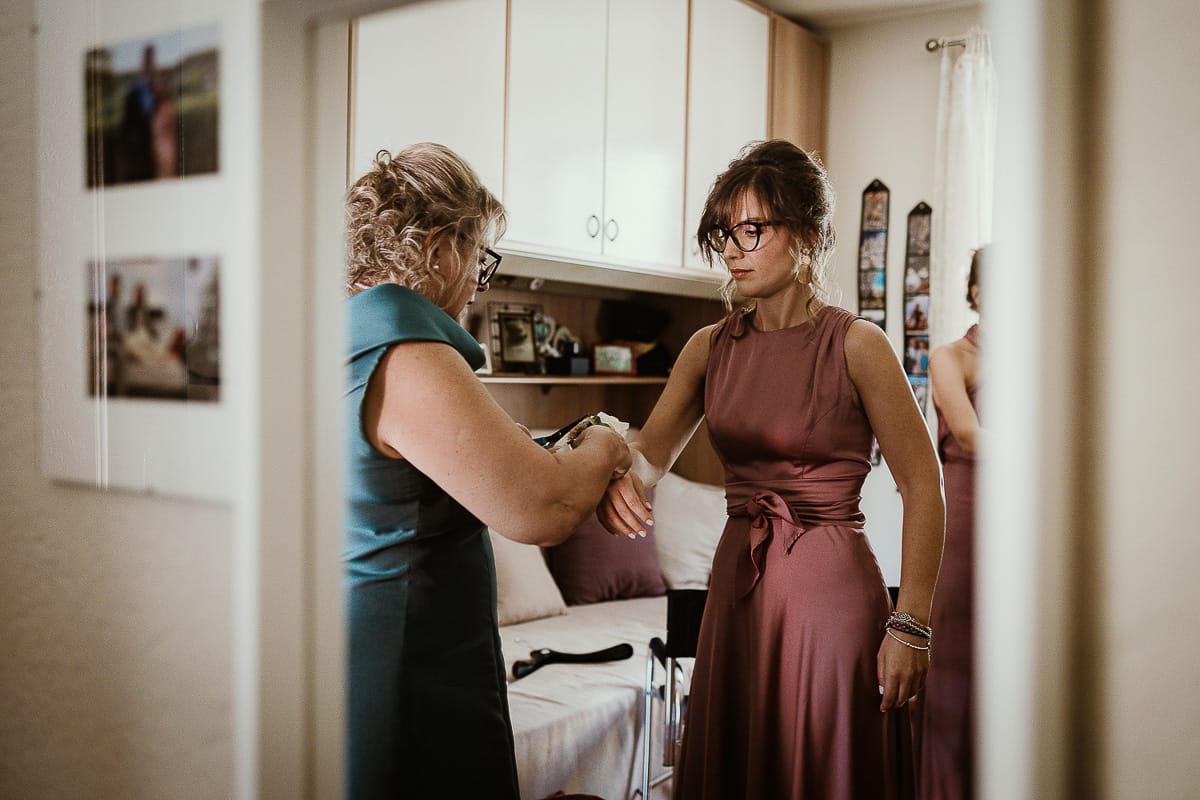Fotografo matrimonio Torino. Matrimonio eco-consapevole a Cascina Ranverso. Preparazione della sposa a Chieri. mamma della sposa mette il corsage ad una delle testimoni