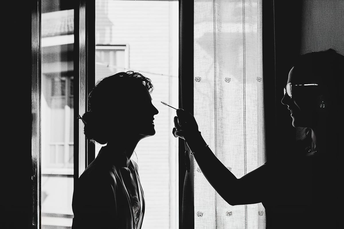 Fotografo matrimonio Torino. Matrimonio eco-consapevole a Cascina Ranverso. Preparazione della sposa a Chieri. Make-up silhouette in bianco e nero di fronte alla finestra