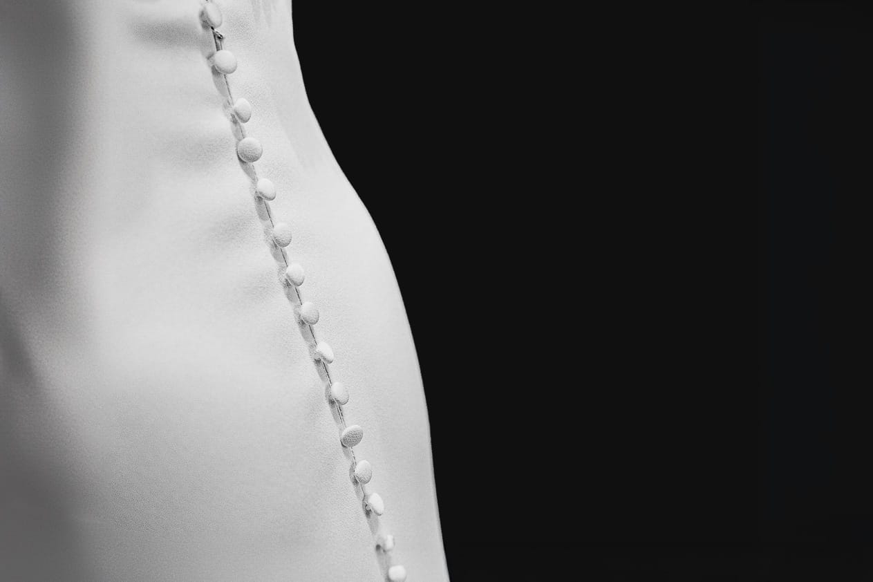 Fotografo matrimonio Torino. Matrimonio eco-consapevole a Cascina Ranverso. Preparazione della sposa a Chieri. Dettaglio dell'abito della sposa con la fila di bottoncini
