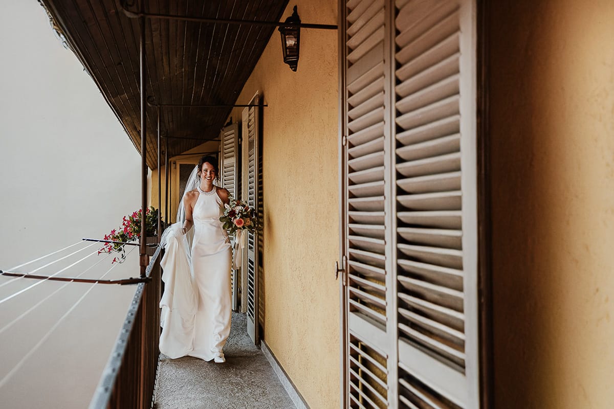 Fotografo matrimonio Torino. Matrimonio eco-consapevole a Cascina Ranverso. Preparazione della sposa a Chieri. Sposa sul balcone mentre esce dalla casa di ringhiera.