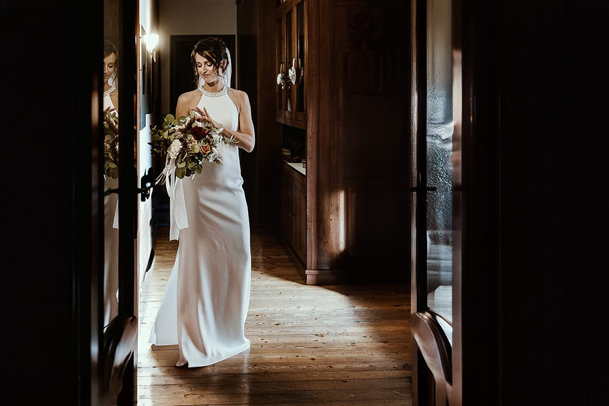 Fotografo matrimonio Torino. Matrimonio eco-consapevole a Cascina Ranverso. Preparazione della sposa a Chieri. Sposa riflessa nel vetro di una porta,