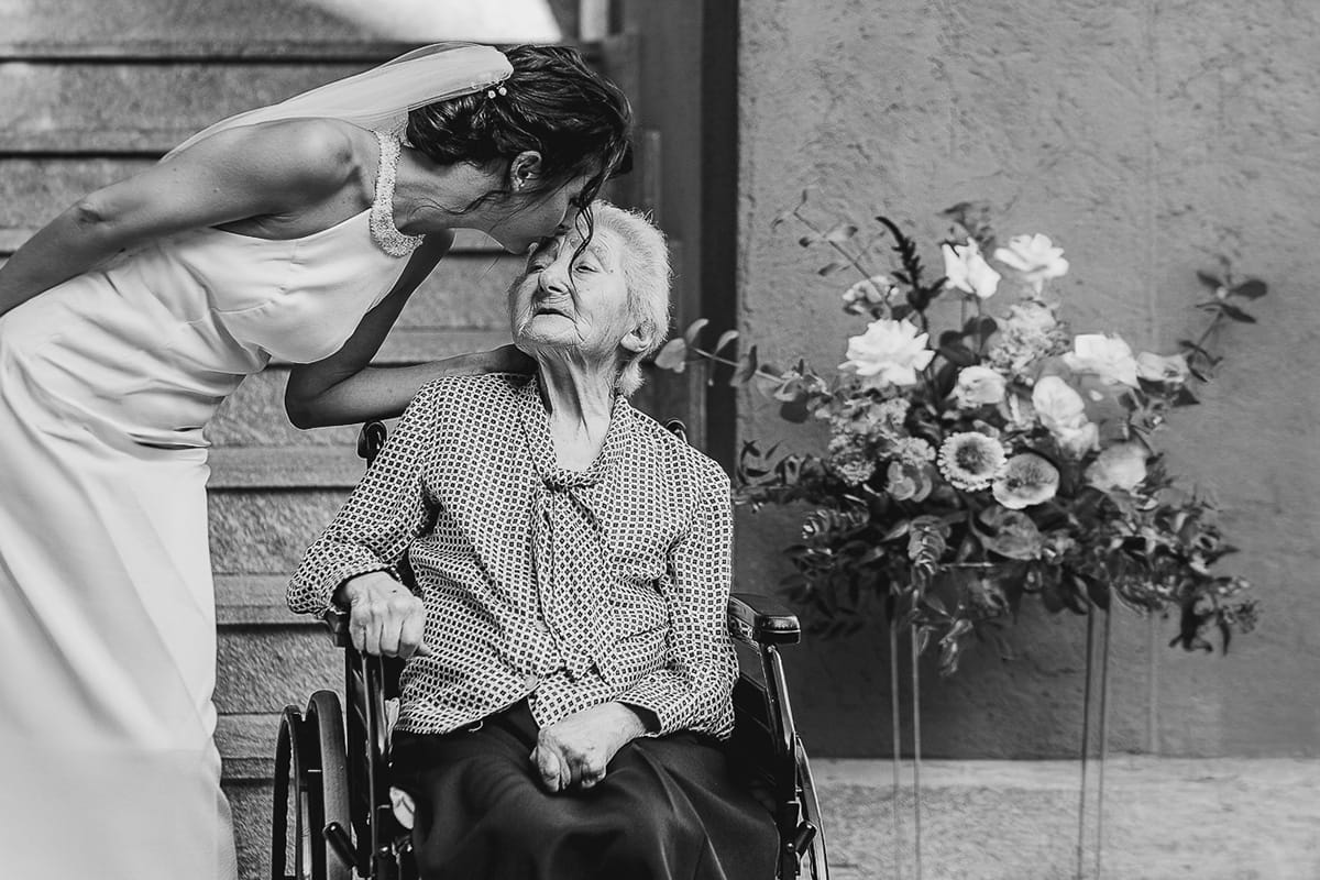 Fotografo matrimonio Torino. Matrimonio eco-consapevole a Cascina Ranverso. Preparazione della sposa a Chieri. Sposa bacia la nonna sulla sedia a rotelle Bianco e nero.