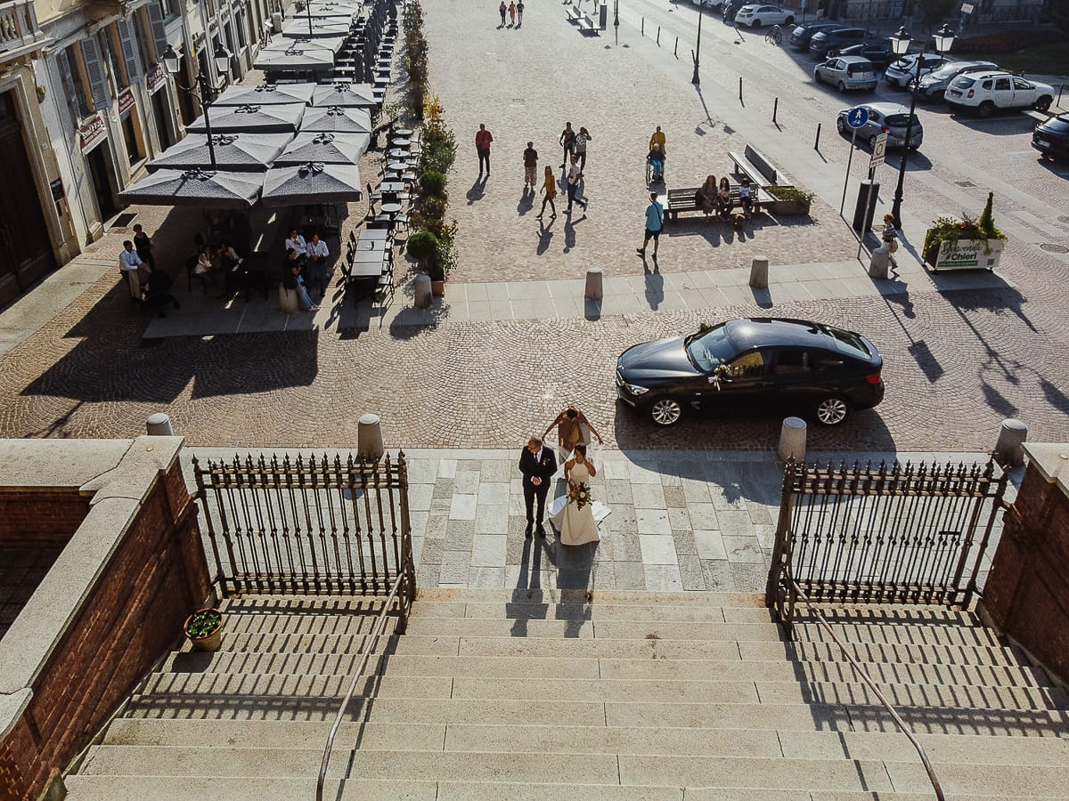 Fotografo matrimonio Torino. Matrimonio eco-consapevole a Cascina Ranverso. Cerimonia a Chieri nella chiesa dei Santi Bernardino e Rocco. Sposa e padre fuori dall'auto. Amica sistema il velo della sposa. Foto dal drone