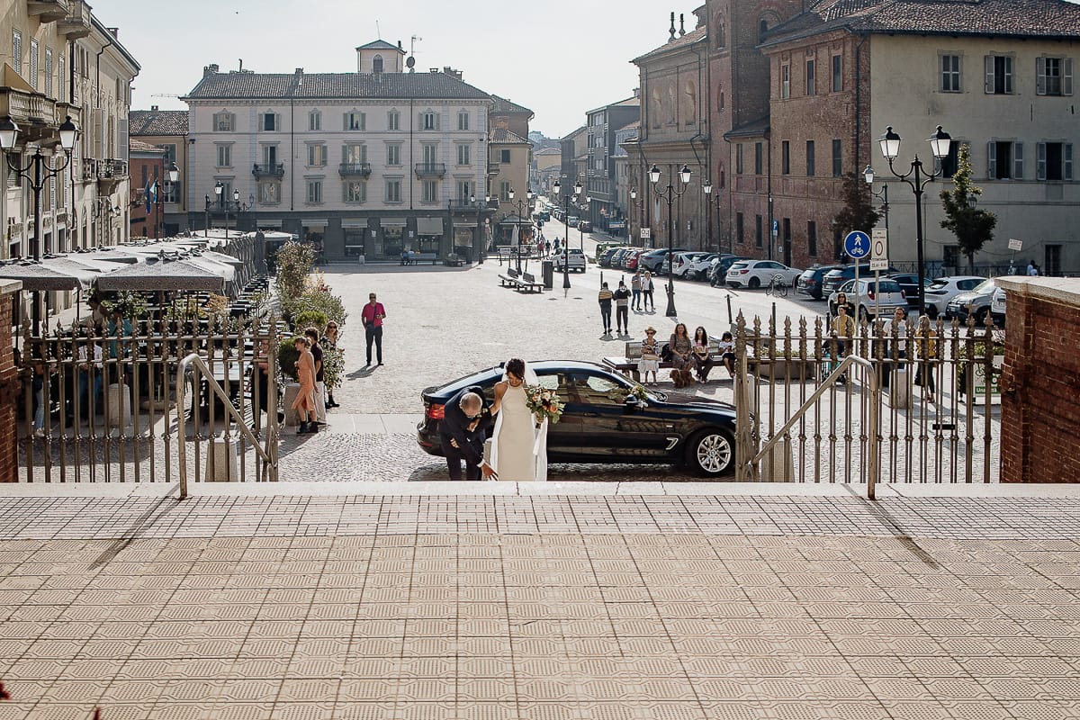 Fotografo matrimonio Torino. Matrimonio eco-consapevole a Cascina Ranverso. Cerimonia a Chieri nella chiesa dei Santi Bernardino e Rocco. Sposa e padre fuori dall'auto. Padre sistema il velo della sposa.