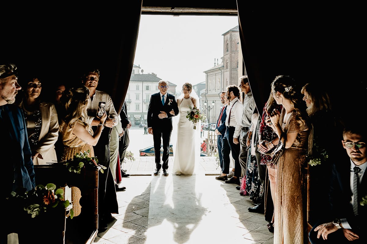 Fotografo matrimonio Torino. Matrimonio eco-consapevole a Cascina Ranverso. Cerimonia a Chieri nella chiesa dei Santi Bernardino e Rocco. Sposa e padre entrano in chiesa.