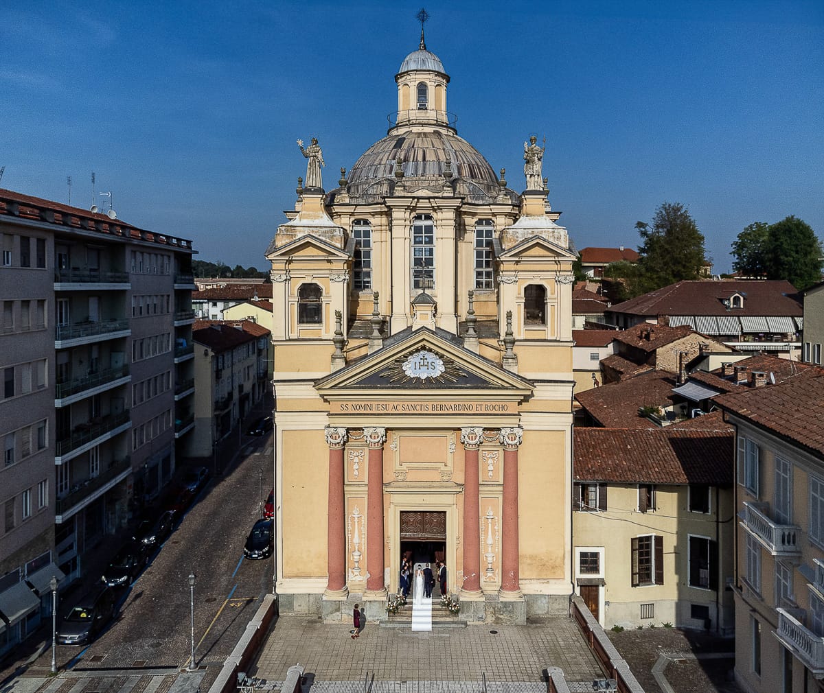 Fotografo matrimonio Torino. Matrimonio eco-consapevole a Cascina Ranverso. Cerimonia a Chieri nella chiesa dei Santi Bernardino e Rocco. Sposa e padre fuori dall'auto. Entrano in chiesa. panoramica dal drone.