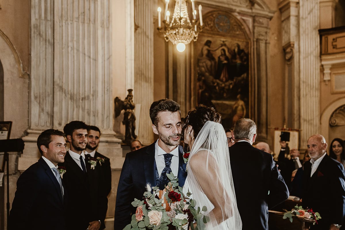 Fotografo matrimonio Torino. Matrimonio eco-consapevole a Cascina Ranverso. Cerimonia a Chieri nella chiesa dei Santi Bernardino e Rocco. Sposa bacia lo sposo.