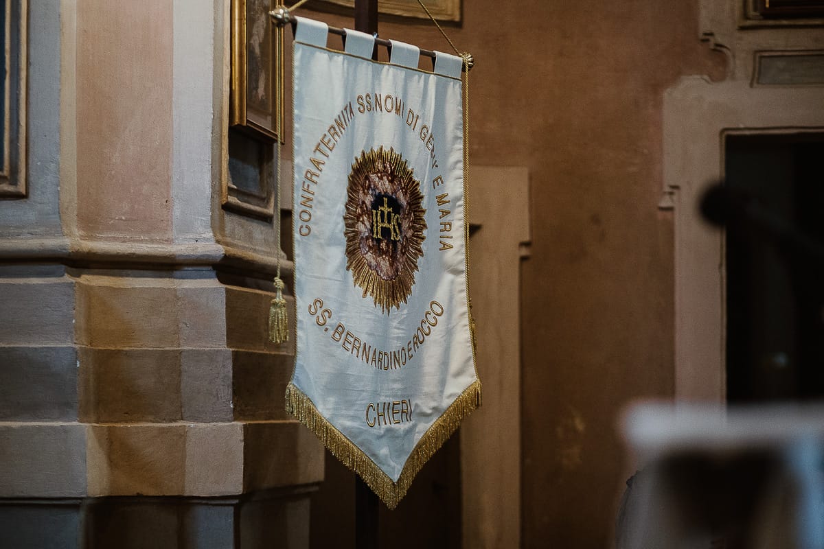 Fotografo matrimonio Torino. Matrimonio eco-consapevole a Cascina Ranverso. Cerimonia a Chieri nella chiesa dei Santi Bernardino e Rocco. Messa. Gonfalone della chiesa.