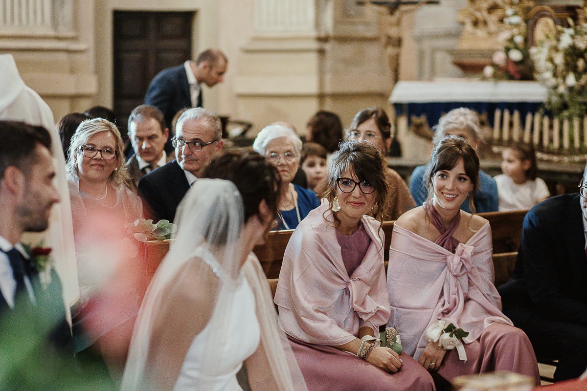 Fotografo matrimonio Torino. Matrimonio eco-consapevole a Cascina Ranverso. Cerimonia a Chieri nella chiesa dei Santi Bernardino e Rocco. Messa.Sposa guarda le testimoni