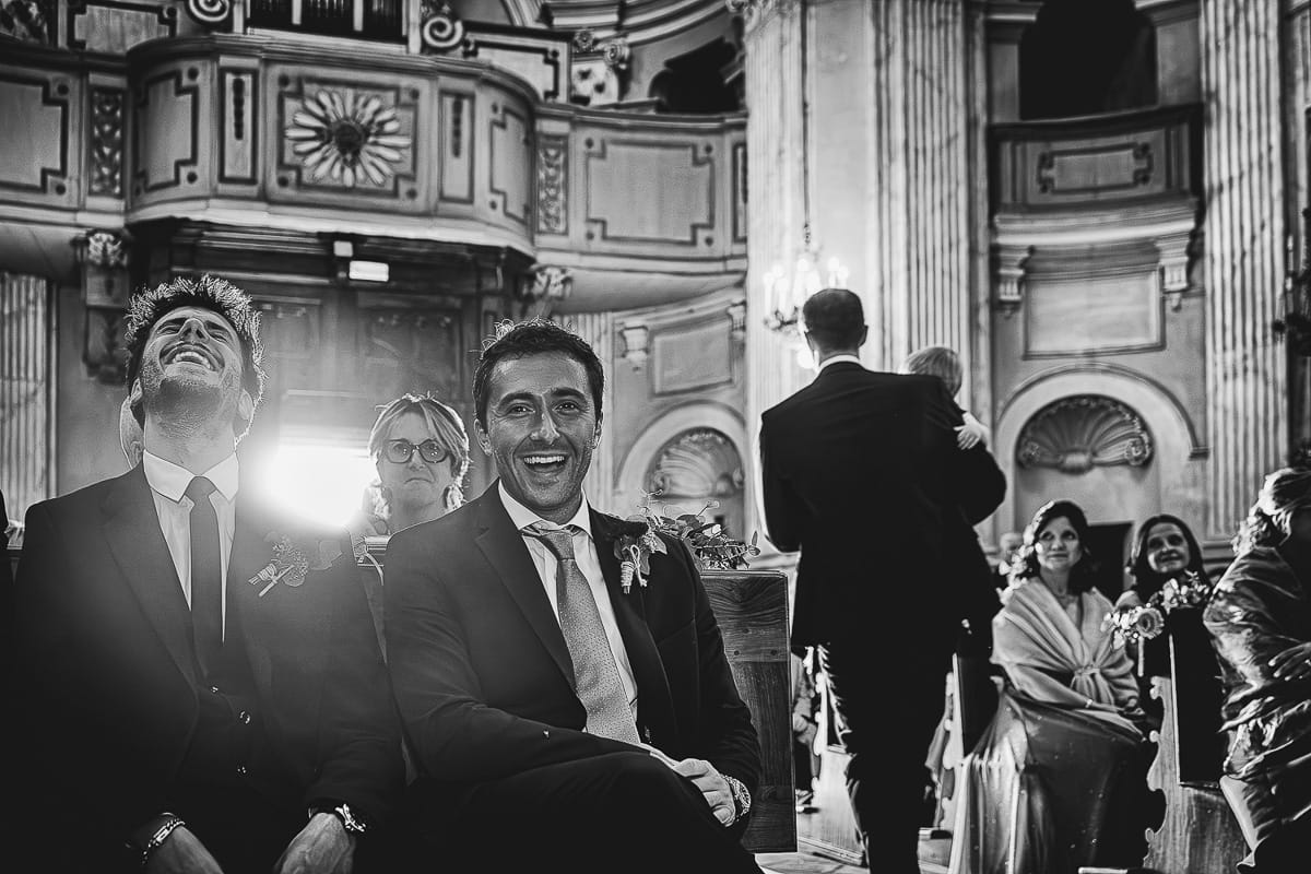 Fotografo matrimonio Torino. Matrimonio eco-consapevole a Cascina Ranverso. Cerimonia a Chieri nella chiesa dei Santi Bernardino e Rocco. Messa.I testimoni dello sposo ridono