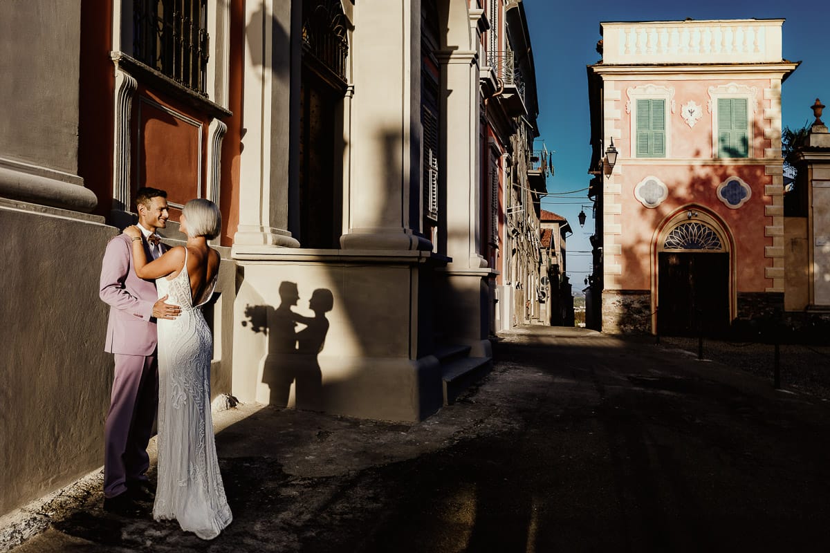 Matrimonio boho-chic da favola nel Monferrato. Fotografo matrimonio Monferrato. matrimonio a Molare (AL). Servizio fotografico di coppia degli sposi. sposi si baciano. Il sole proietta la loro ombra sul muro.