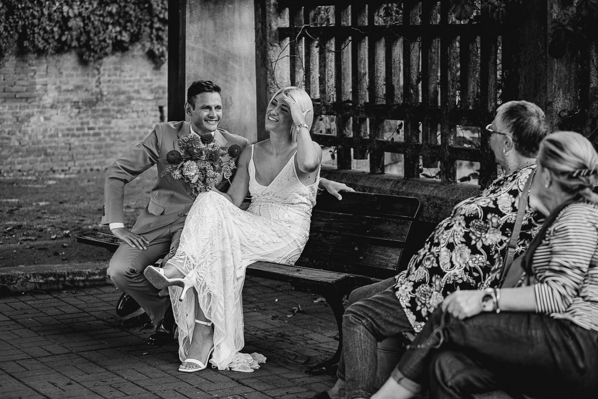 Matrimonio boho-chic da favola nel Monferrato. Fotografo matrimonio Monferrato. matrimonio a Molare (AL). Servizio fotografico di coppia degli sposi. Sposi seduti su di una panchina chiacchierano con le signore del paese.