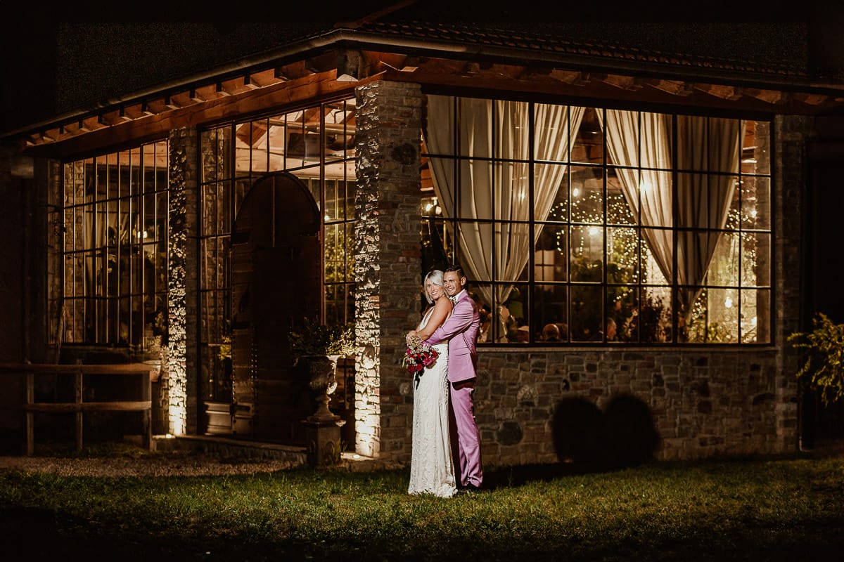 Matrimonio boho-chic da favola nel Monferrato. Fotografo matrimonio Monferrato. Matrimonio a Molare. Agriturismo "A Modo Mio" Ricevimento. Ritratto degli sposi di notte fuori dalla sala illuminata. uso del flash esterno.