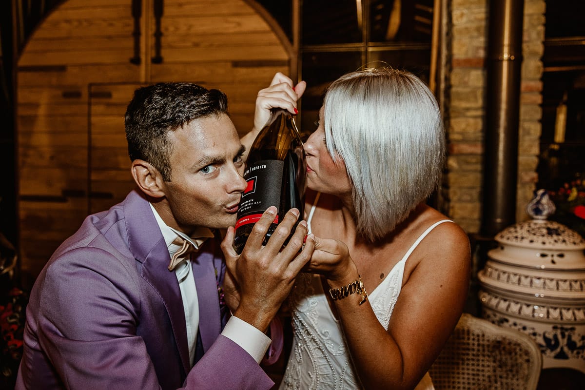 Matrimonio boho-chic da favola nel Monferrato. Fotografo matrimonio Monferrato. Matrimonio a Molare. Agriturismo "A Modo Mio" Ricevimento. Sposi baciano la bottiglia di vino Magnum