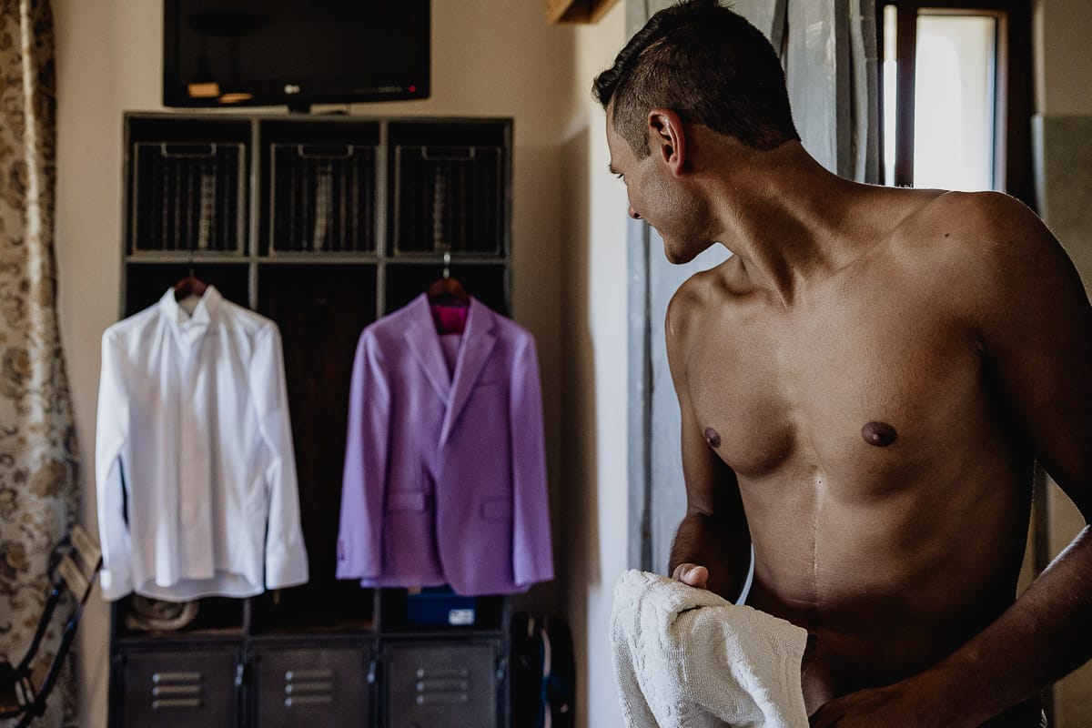Matrimonio boho-chic da favola nel Monferrato. Matrimonio a Molare. Agriturismo "A Modo Mio". Preparazione dello sposo. Sposo uscendo dal bagno guarda il suo abito e la sua camicia.