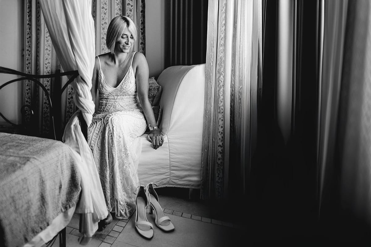 Matrimonio boho-chic da favola nel Monferrato. Matrimonio a Molare. Agriturismo "A Modo Mio". Preparazione della sposa. Sposa seduta su di una poltrona si appresta a indossare le scarpe