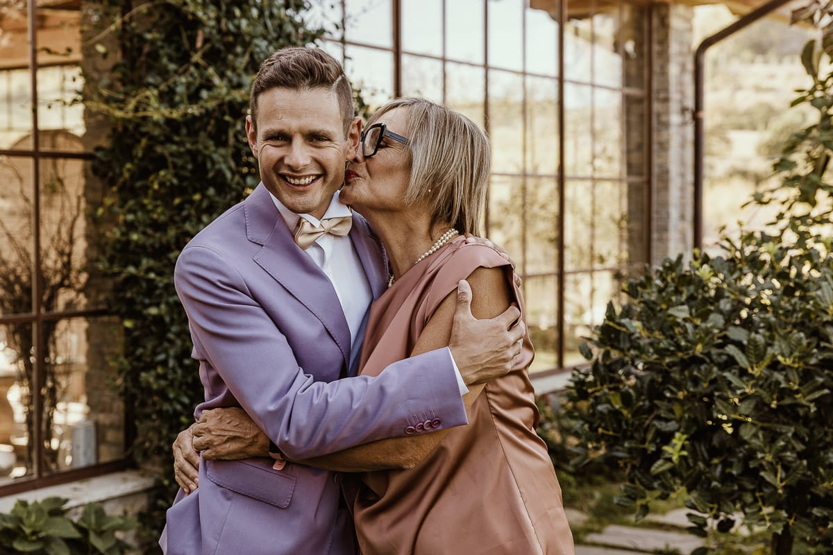 Matrimonio boho-chic da favola nel Monferrato. Matrimonio a Molare. Agriturismo "A Modo Mio". Preparazione dello sposo. Ritratto dello sposo in giardino. la mamma lo bacia