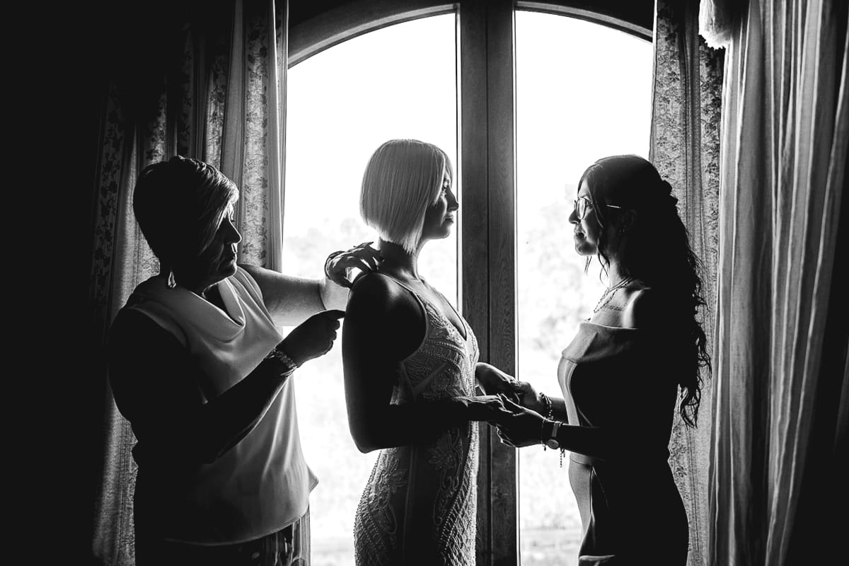 Matrimonio boho-chic da favola nel Monferrato. Matrimonio a Molare. Agriturismo "A Modo Mio". Preparazione della sposa. Vestizione. Silhouette in controluce alla finestra della sposa con la mamma e la testimone.