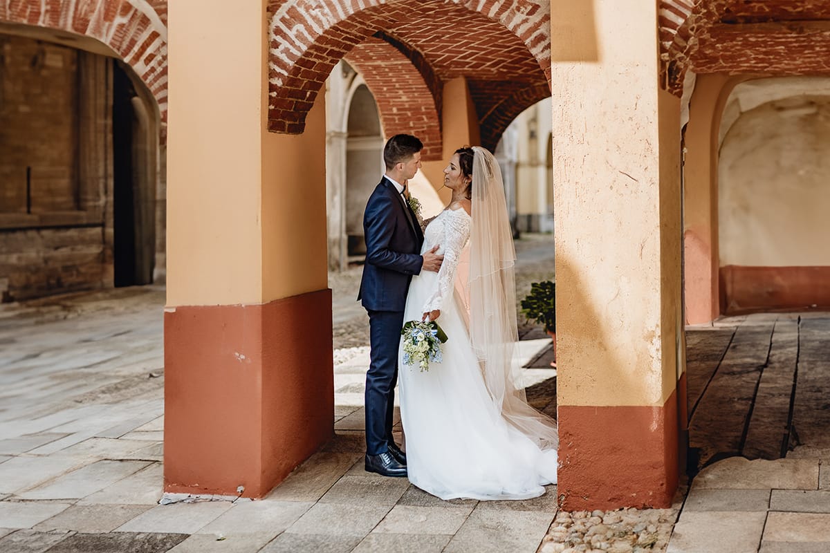 Fotografo matrimonio Torino | Tenuta La Michelina | Pinerolo. Ritratto di coppia degli sposi. Sposi sotto nel centro storico di Poirino. Sposi sotto un portico medievale si guardano.
