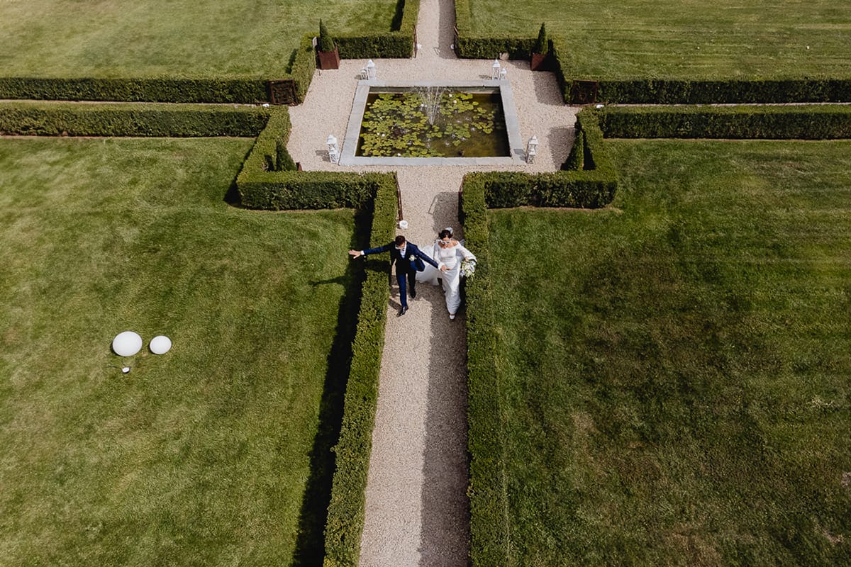 Fotografo matrimonio Torino | Tenuta La Michelina | Pinerolo. Sposi corrono nel vialetto del giardino all'italiana, con gli occhiali da sole a forma di cuore. foto aerea dal drone.