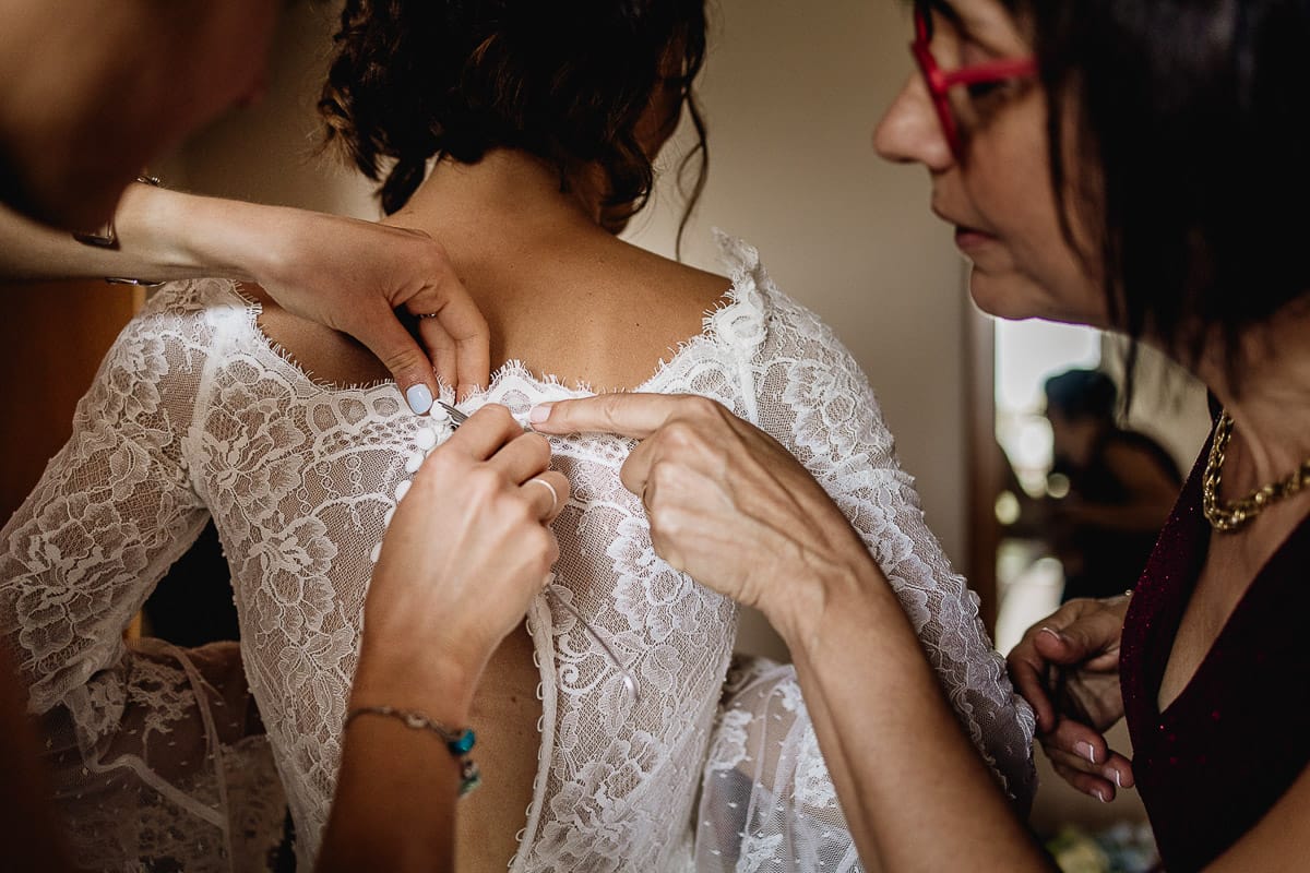 Fotografo matrimonio Torino | Tenuta La Michelina | Pinerolo. Preparazione della sposa. Vestizione. Sorella abbottona l'abito e mamma controlla