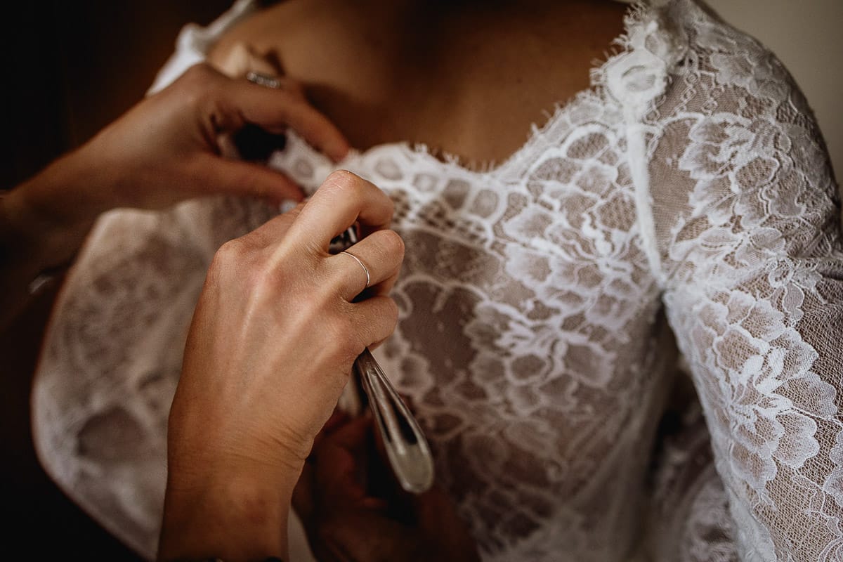 Fotografo matrimonio Torino | Tenuta La Michelina | Pinerolo. Preparazione della sposa. Vestizione. sorella abbottona l'abito aiutandosi con una forchetta