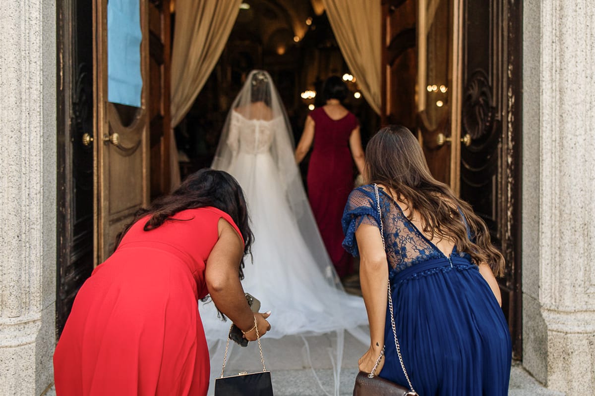 Fotografo matrimonio Torino | Tenuta La Michelina | Pinerolo. Cerimonia religiosa nella chiesa di Santa Maria Maggiore di Poirino. Ritratto della sposa che entra in chiesa con la mamma ripresa da dietro con le amiche che aggiustano il velo.