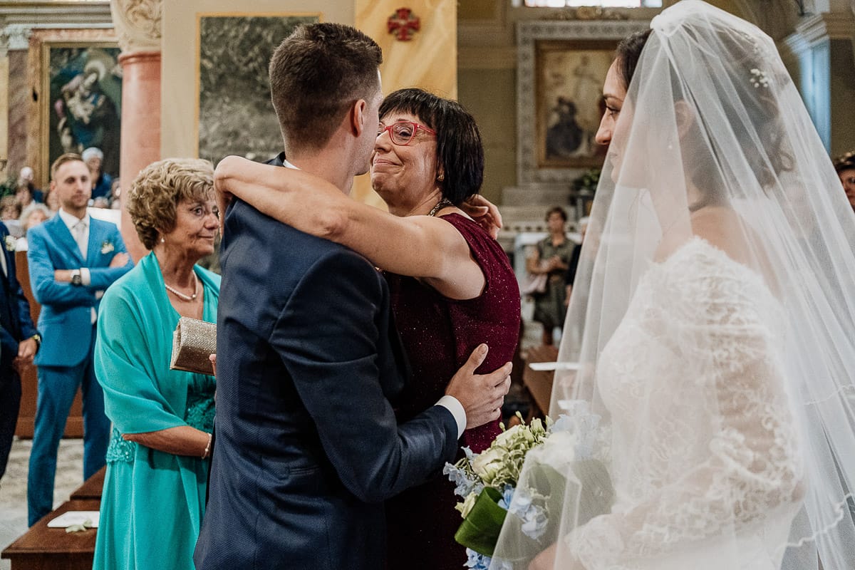 Fotografo matrimonio Torino | Tenuta La Michelina | Pinerolo. Cerimonia religiosa nella chiesa di Santa Maria Maggiore di Poirino. mamma della sposa abbraccia lo sposo