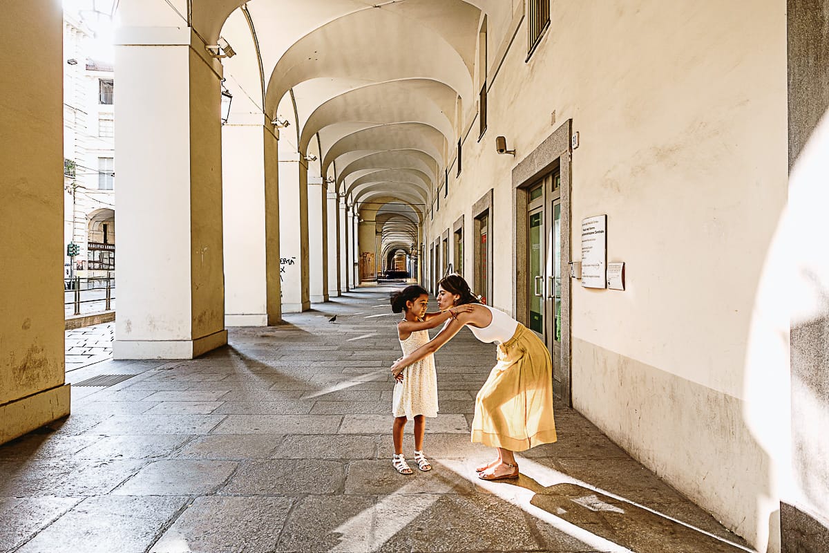 Fotografia di famiglia in vacanza a Torino: mamma abbraccia la bambina più piccola in via Po.