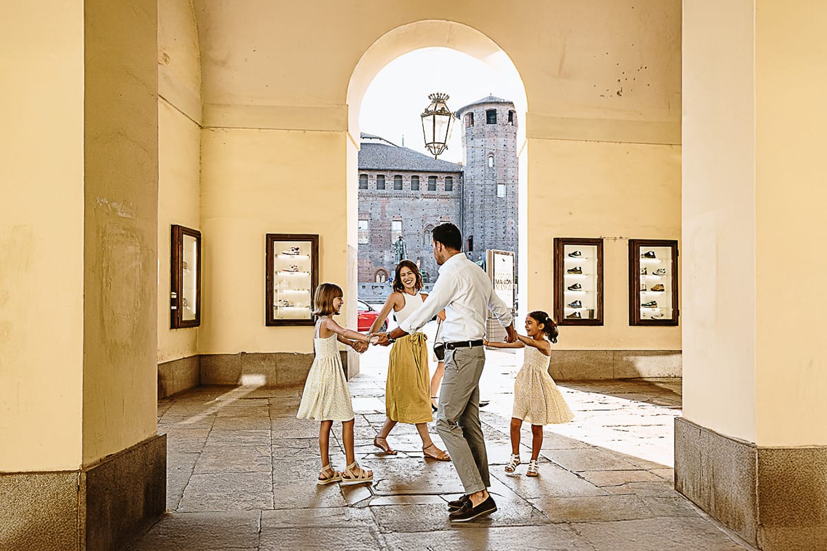 Fotografia di famiglia in vacanza a Torino: famiglia americana fa il girotondo. Sullo sfondo, attraverso l'arco di un portico si scorge il castello medievale di piazza Castello.