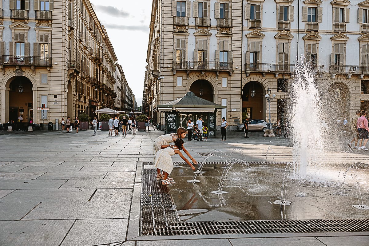 Fotografia di famiglia in vacanza a Torino: bambine incuriosite dalle fontane di piazza Castello