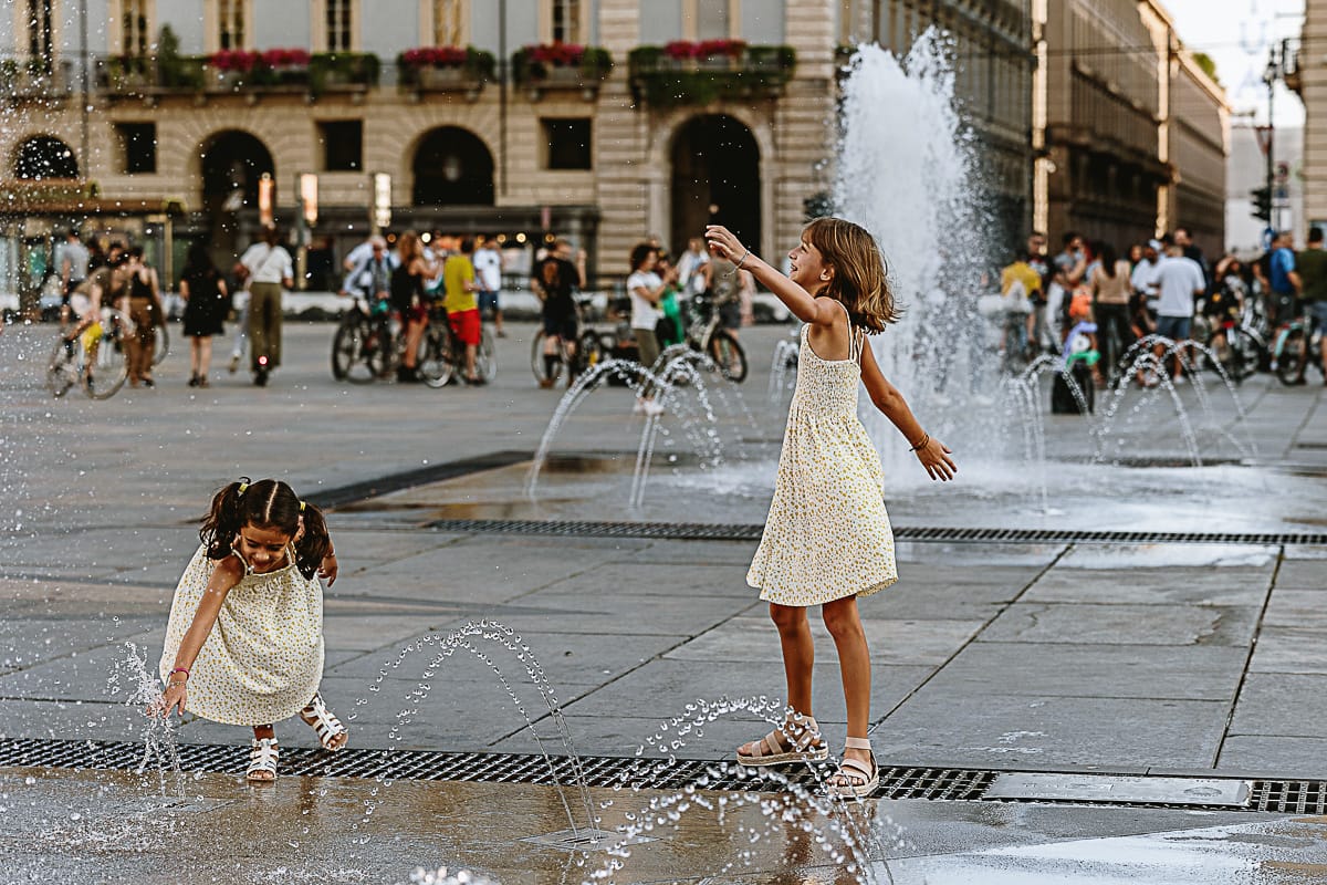 Fotografia di famiglia in vacanza a Torino: bambine giocano con l'acqua delle fontane di piazza Castello