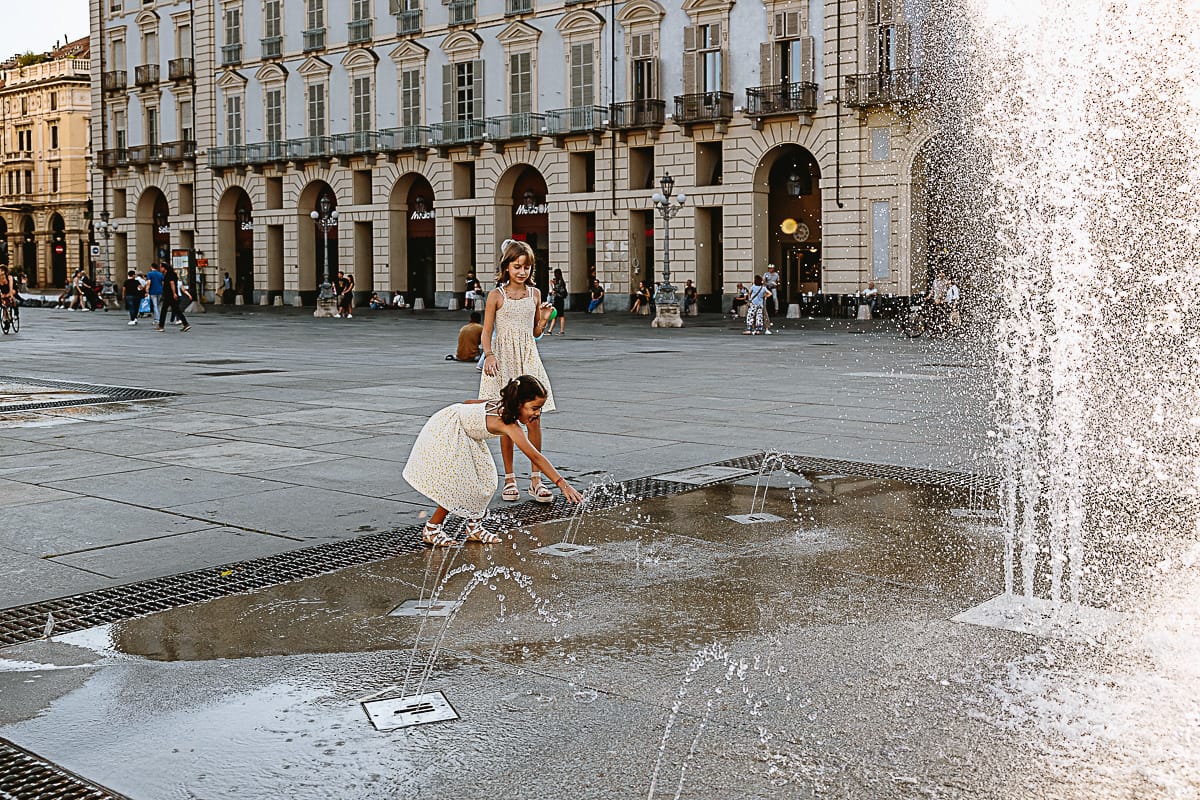 Fotografia di famiglia in vacanza a Torino: bambine giocano con l'acqua delle fontane di piazza Castello