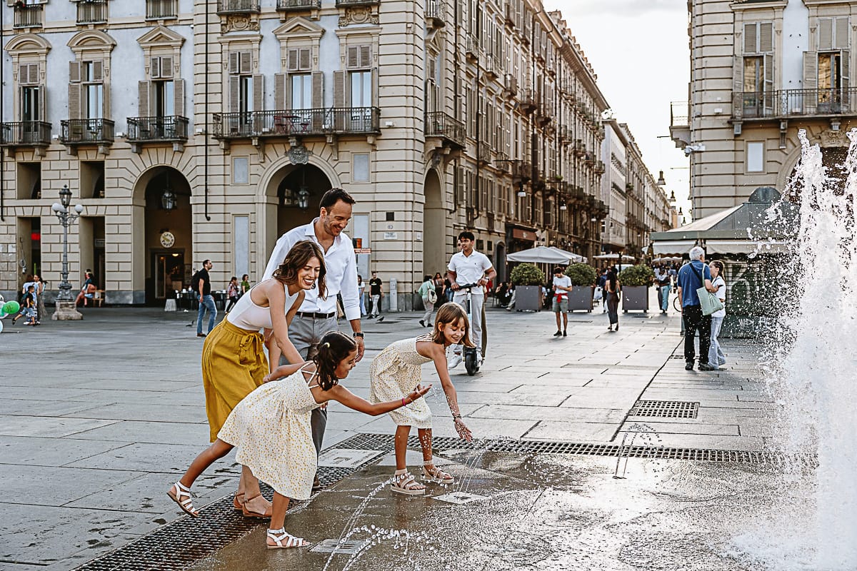 Fotografia di famiglia in vacanza a Torino: bambine giocano con l'acqua delle fontane di piazza Castello