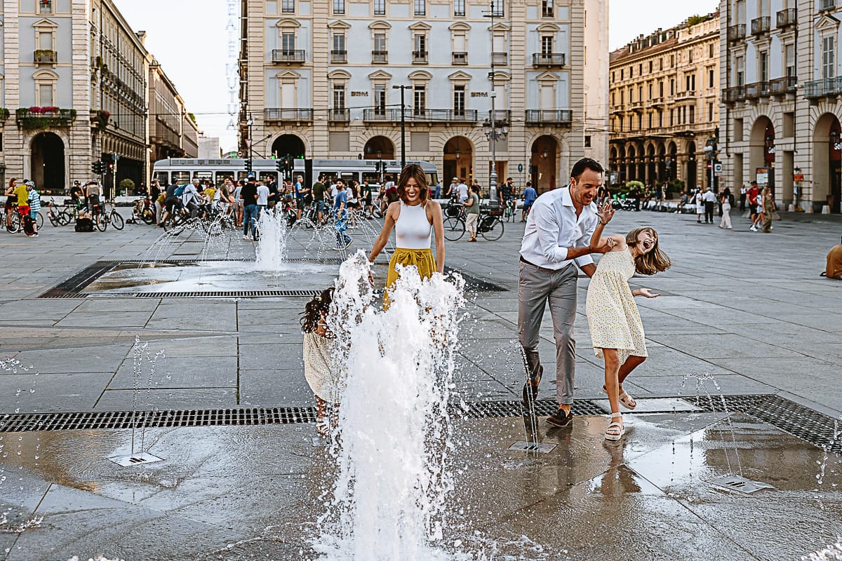 Fotografia di famiglia in vacanza a Torino: bambine giocano con l'acqua delle fontane di piazza Castello
